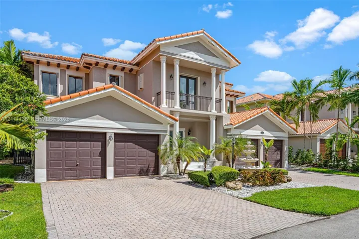 Two-story stucco exterior featuring a tiled roof, multi-bay garage, covered entryway with classical columns, second-level balcony, and decorative stone fountain
