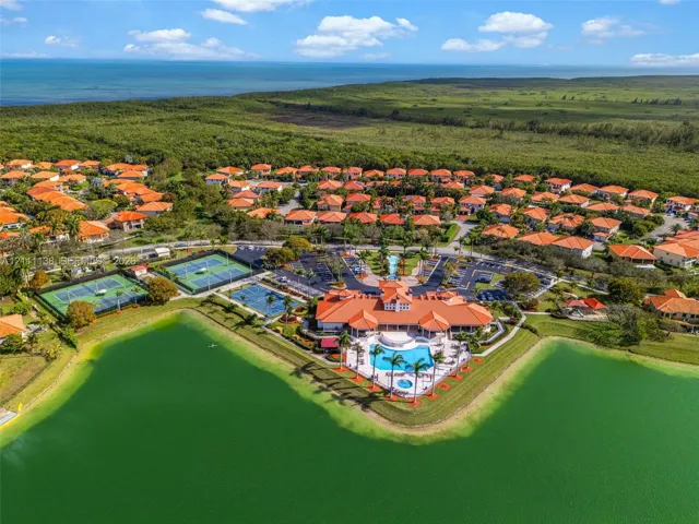 Aerial perspective of a community clubhouse featuring a swimming pool, multiple tennis courts, shoreline access, and proximity to the coast