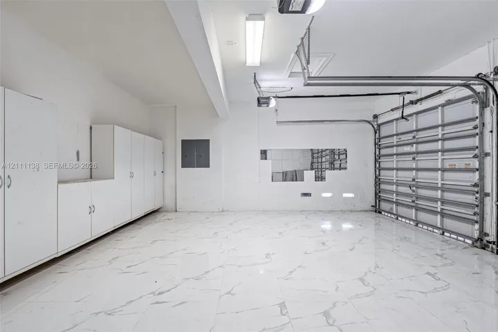 Garage featuring expansive stone-finish flooring, extensive white built-in cabinetry, overhead task lighting, and an automated sectional door