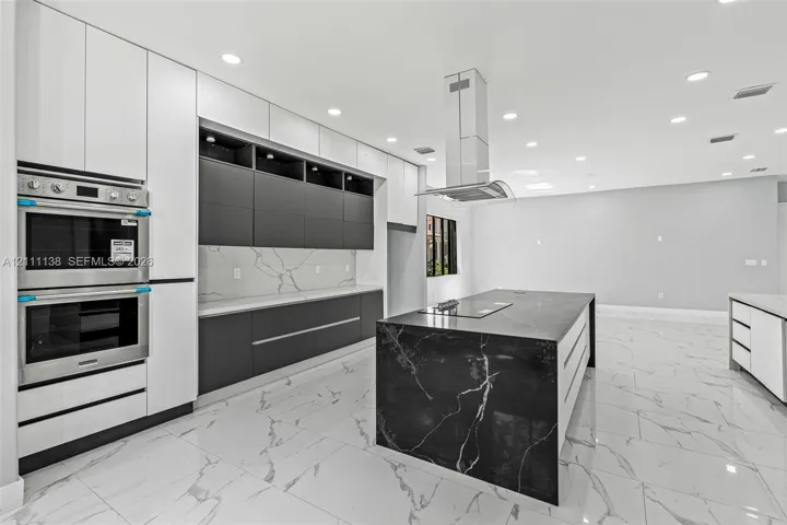 Kitchen featuring flat-panel cabinetry, a waterfall-edge island with an integrated cooktop, quartz countertops with a veined pattern, a stainless steel double wall oven, and recessed lighting
