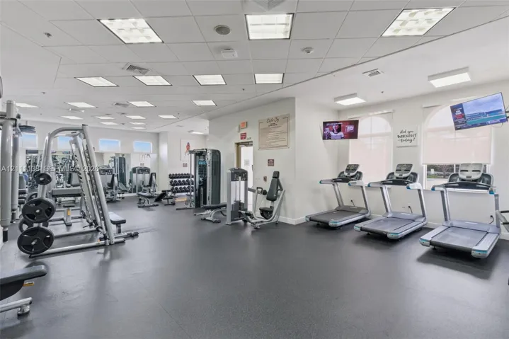 Fitness facility featuring rubberized flooring, recessed grid lighting, multiple treadmills, and wall-mounted televisions
