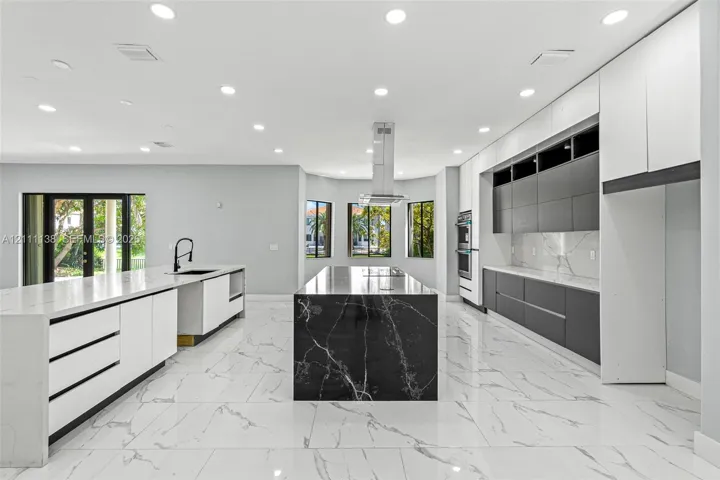 Modern kitchen featuring flat-panel cabinetry, a central island with a contrasting stone finish, stone-surface countertops, tile flooring, and a stainless steel ceiling-mounted vent hood