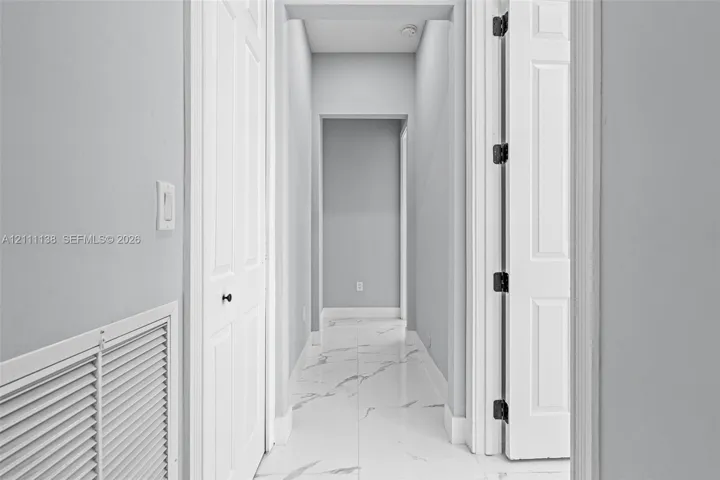 Hallway featuring white veined tile flooring, solid core two-panel doors, and neutral wall tones