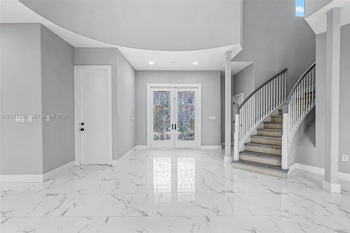 Foyer featuring large-format veined tile flooring, a curved staircase with white spindles, high ceilings with recessed lighting, and double-entry doors