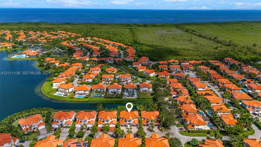 Aerial perspective of a multi-level residence featuring a clay tile roof, paved driveway, and water frontage with bulkhead