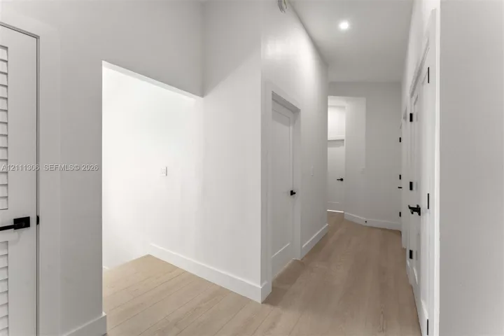 Hallway featuring wood-finish flooring, shaker-style interior doors, matte black hardware, and recessed lighting