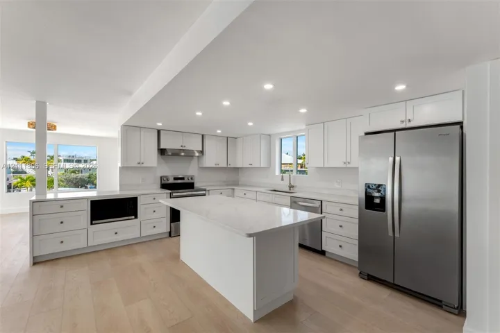 Kitchen featuring white shaker-style cabinetry, quartz countertops, a central island, wood-finish flooring, and stainless steel appliances