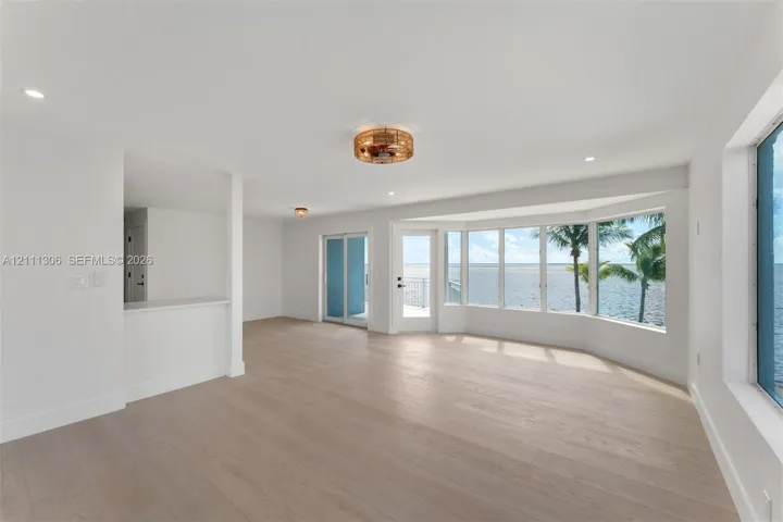 Open-concept interior featuring light-toned wood-finish flooring, a bay window with water frontage, recessed lighting, and a glass-paneled exterior door