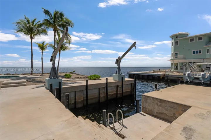 Waterfront concrete dock featuring dual boat lifts, integrated swimming ladder, and expansive open-water frontage