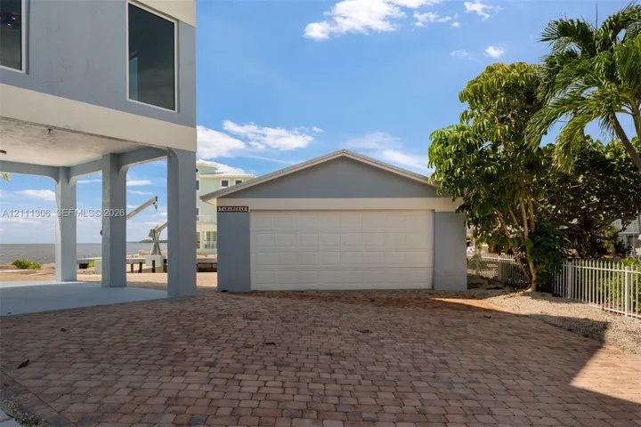 Detached garage with a multi-panel door, paver driveway, stilt-construction foundation, and coastal location