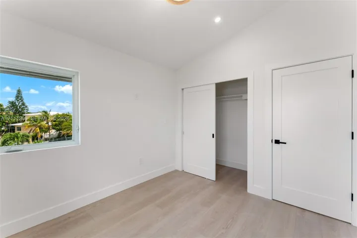 Interior space featuring vaulted ceilings, light-toned wood-finish flooring, a sliding closet door, and a single-panel interior door with matte black hardware