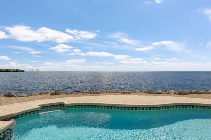 Inground swimming pool with tiled coping, stone-paver pool deck, and natural rock shoreline