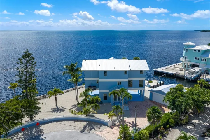 Waterfront residence featuring a metal roof, elevated structural design, private dock, paved driveway, and mature landscaping