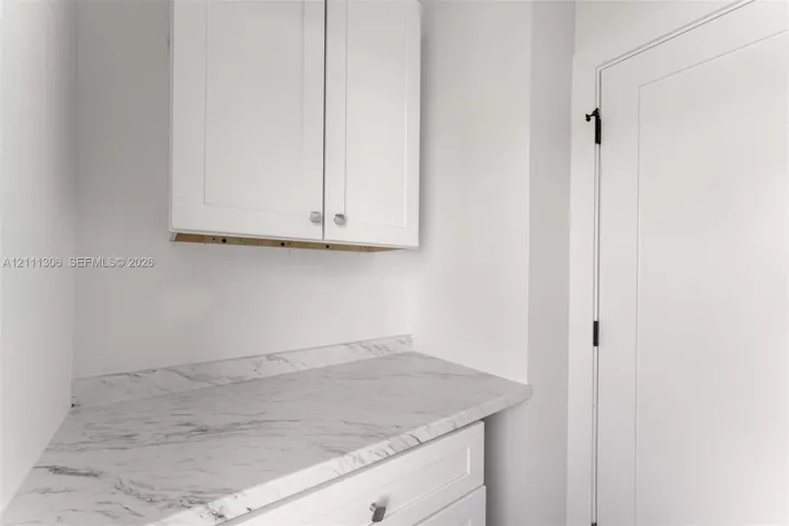 Shaker-style white cabinetry, stone-finish countertop with matching backsplash, and solid-core door with matte black hardware