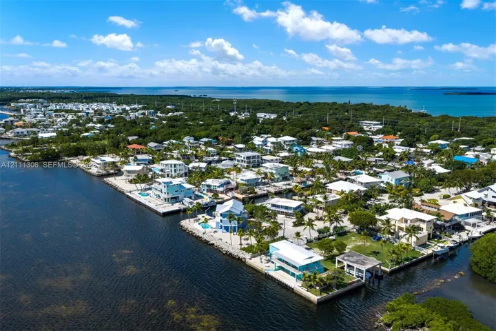 Aerial perspective of a coastal property featuring direct waterfront access, a private boat dock, a sea wall, and expansive open-water scenery