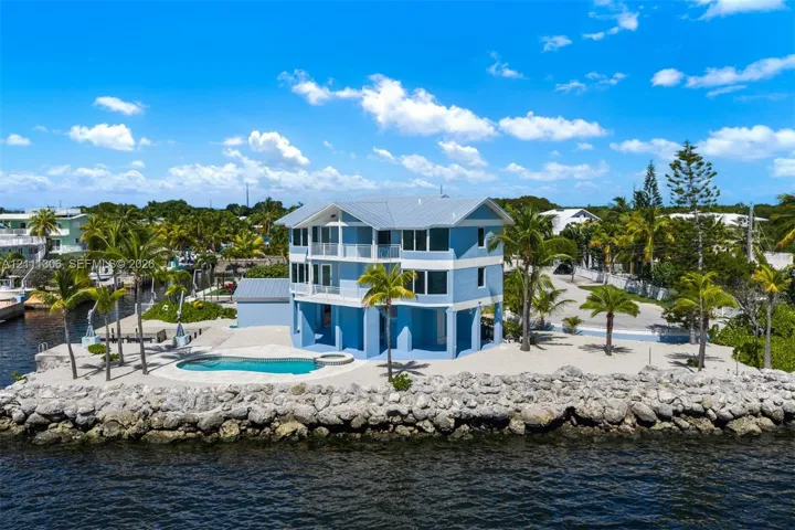 Multi-level coastal residence featuring metal roofing, private swimming pool with integrated spa, concrete sea wall, and expansive open-air balconies