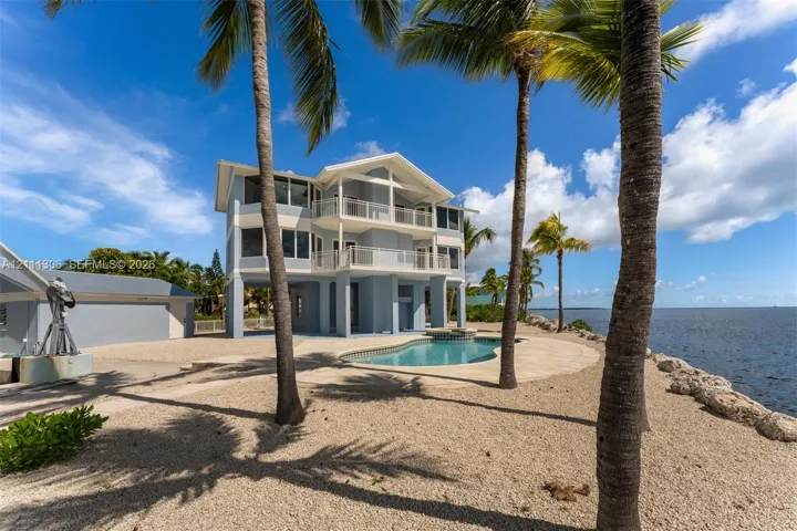 Stilts-elevated residence featuring multi-level covered balconies, an in-ground pool, and water-side hardscaping