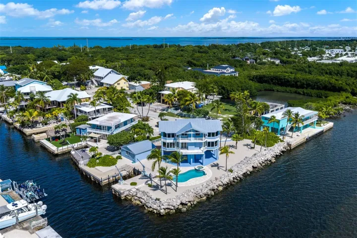 Waterfront residence featuring a private pool with built-in spa, multiple levels of balconies, a dedicated boat lift, and seawall-protected grounds
