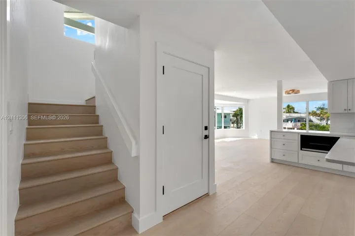 Staircase featuring wood-finish treads and white railing, wood-finish flooring, white shaker-style cabinetry, and large windows