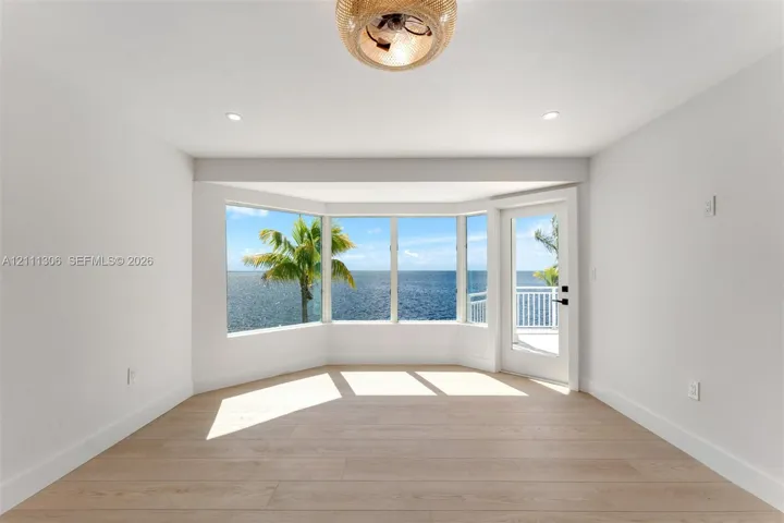 Bay window with water backdrop, wood-finish flooring, recessed lighting, woven-texture ceiling fixture, and glass-paneled exterior door