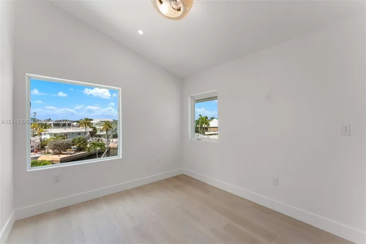 Bright room featuring a vaulted ceiling, wood-finish flooring, recessed lighting, and large windows with water and palm tree scenery