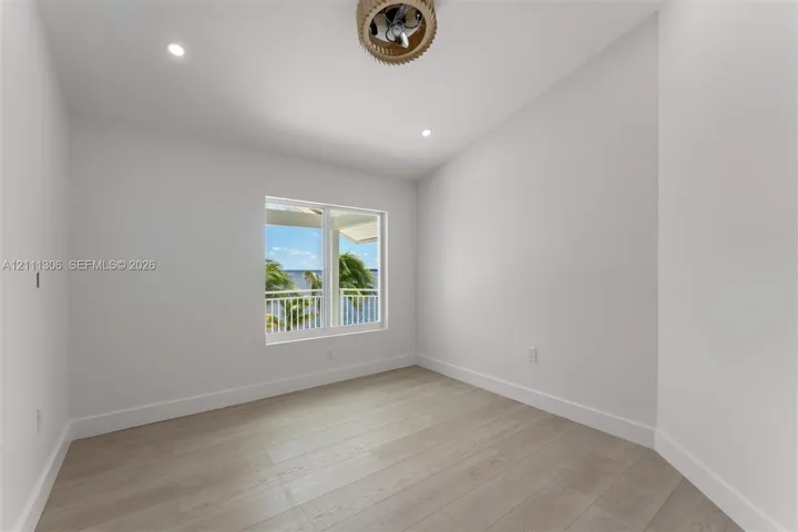 Neutral interior space featuring wood-finish flooring, recessed lighting, and a drum-style ceiling fan, with a window framing water and palm tree scenery