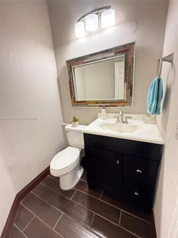 Dark-toned cabinetry with a white integrated countertop, wood-finish tile flooring, three-light vanity fixture, and brushed metal hardware