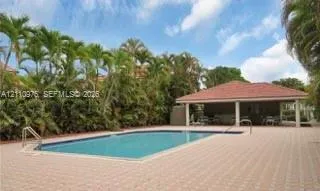In-ground pool with metal handrails surrounded by a spacious paver deck and a covered pavilion featuring a hipped tile roof