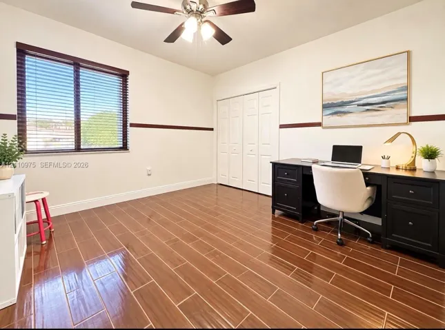 Wood-finish tile flooring, horizontal wall molding, ceiling fan with integrated lighting, and white multi-panel closet doors