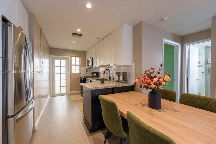 Kitchen featuring white upper cabinetry, dark lower cabinetry, stone-finish countertops, stainless steel refrigerator, and recessed lighting