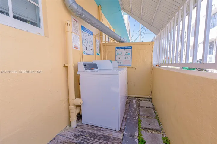 Exterior laundry area featuring a white top-load washer, concrete paver pathway, and metal safety railing