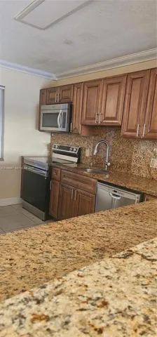 Kitchen featuring raised-panel wood cabinetry, natural stone countertops, stainless steel appliances, and an undermount sink with a gooseneck faucet