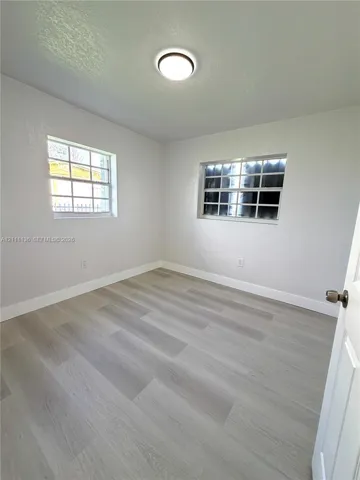 Room featuring neutral walls, wood-finish flooring, two multi-pane windows with security bars, and a flush-mount ceiling light fixture