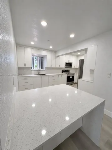 Kitchen featuring white shaker-style cabinetry, quartz countertops, a waterfall-edge island, stainless steel appliances, and recessed lighting