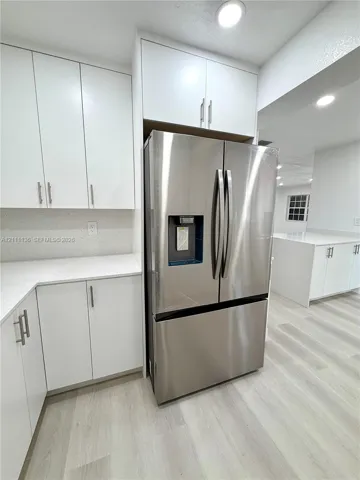 White shaker-style cabinetry with satin nickel pulls, stone-composite countertops, stainless steel French door refrigerator, and wood-finish flooring
