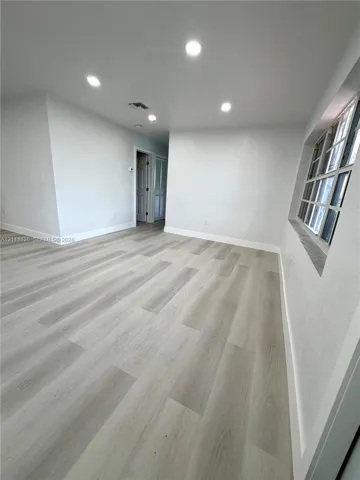 Interior space featuring wood-finish flooring, recessed lighting, neutral wall paint, multi-pane window, and an exterior door with an oval glass insert