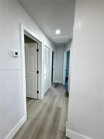 Hallway featuring wood-finish flooring, recessed ceiling lighting, louvered bi-fold doors, and multi-panel interior doors