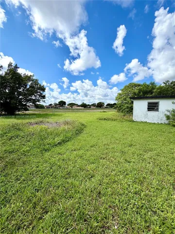 Expansive grass lot featuring a detached structure with a louvered window and chain-link fencing