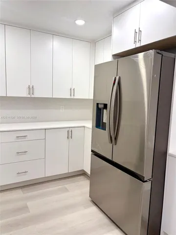 White cabinetry featuring linear hardware, light-toned solid surface countertops, light wood-finish flooring, and a stainless steel French door refrigerator with a built-in water dispenser