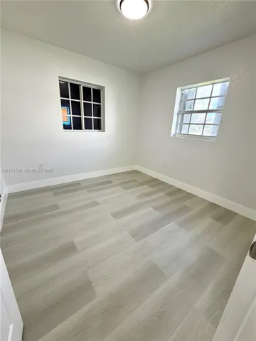 Neutral-toned room featuring wood-finish flooring, white walls, two grid-pane windows, and a flush-mount ceiling light fixture