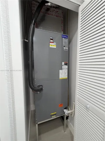 Utility closet housing a vertical HVAC air handler unit with insulated ductwork and a louvered door enclosure