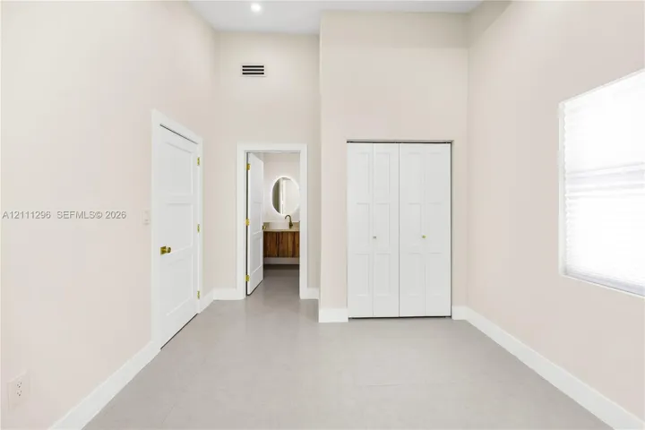 High-ceilinged room featuring neutral wall tones, large-format tile flooring, double-door closet cabinetry, and three-panel interior doors