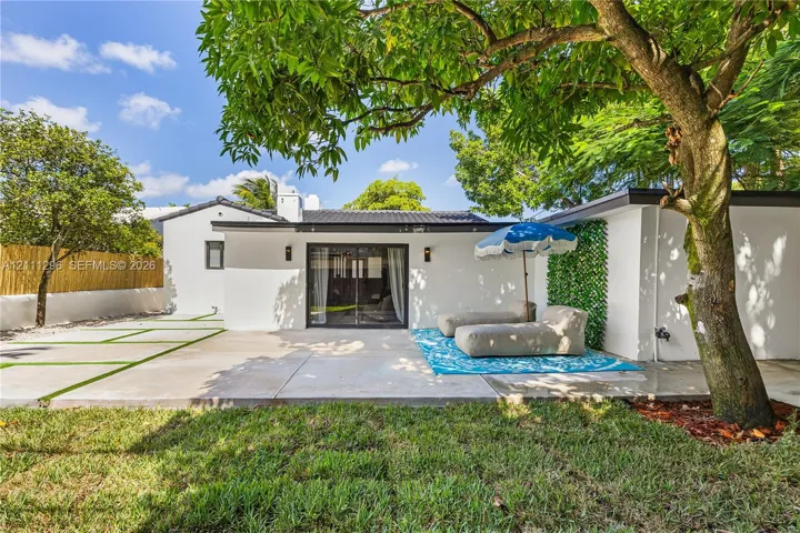 Rear exterior featuring a concrete patio, sliding glass doors, mature trees, a bamboo privacy screen, and exterior wall-mounted lighting