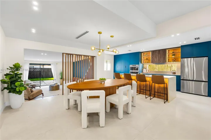 Open-concept kitchen and dining area featuring a central island with integrated stone countertop, modern blue cabinetry, wooden slat room divider, and brushed gold chandelier lighting