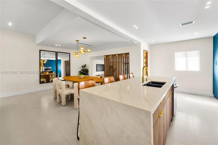 Kitchen island with waterfall countertop, wood-finish cabinetry, brass-toned faucet, recessed lighting, and decorative wood slat partition