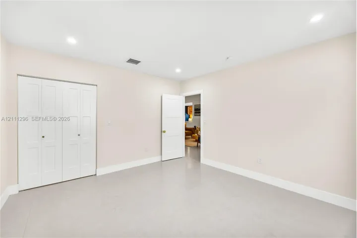 Neutral-toned interior room featuring recessed lighting, a three-panel door, and a white bi-fold closet