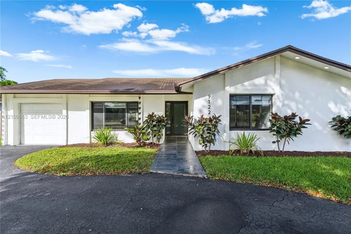 Single-story exterior featuring white stucco siding, a tiled roof, a paved walkway, a multi-pane glass entry door, and an attached garage