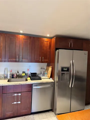 Kitchen area featuring dark-stained wood cabinetry, stone-finish countertops, stainless steel side-by-side refrigerator, under-mount stainless steel sink, and stainless steel dishwasher