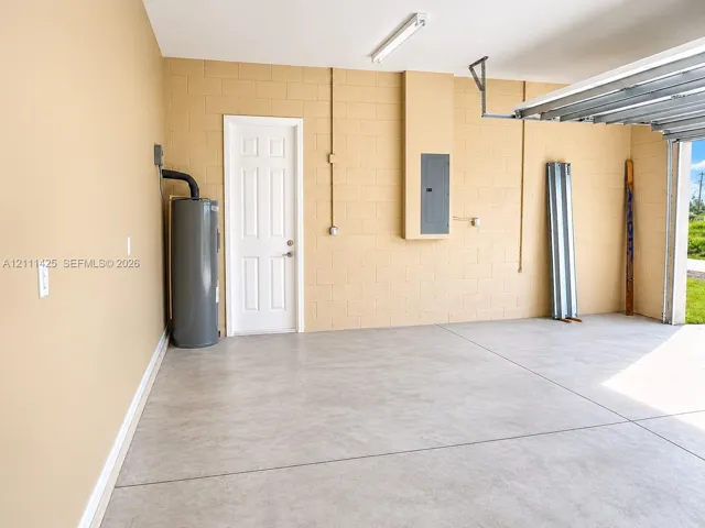 Garage interior featuring finished concrete flooring, painted masonry walls, a utility water heater, and a circuit breaker panel