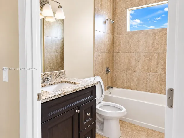 Dark wood-finish cabinetry topped with a stone vanity counter, undermount sink, multi-light fixture, and a tub-shower combination featuring tiled surround